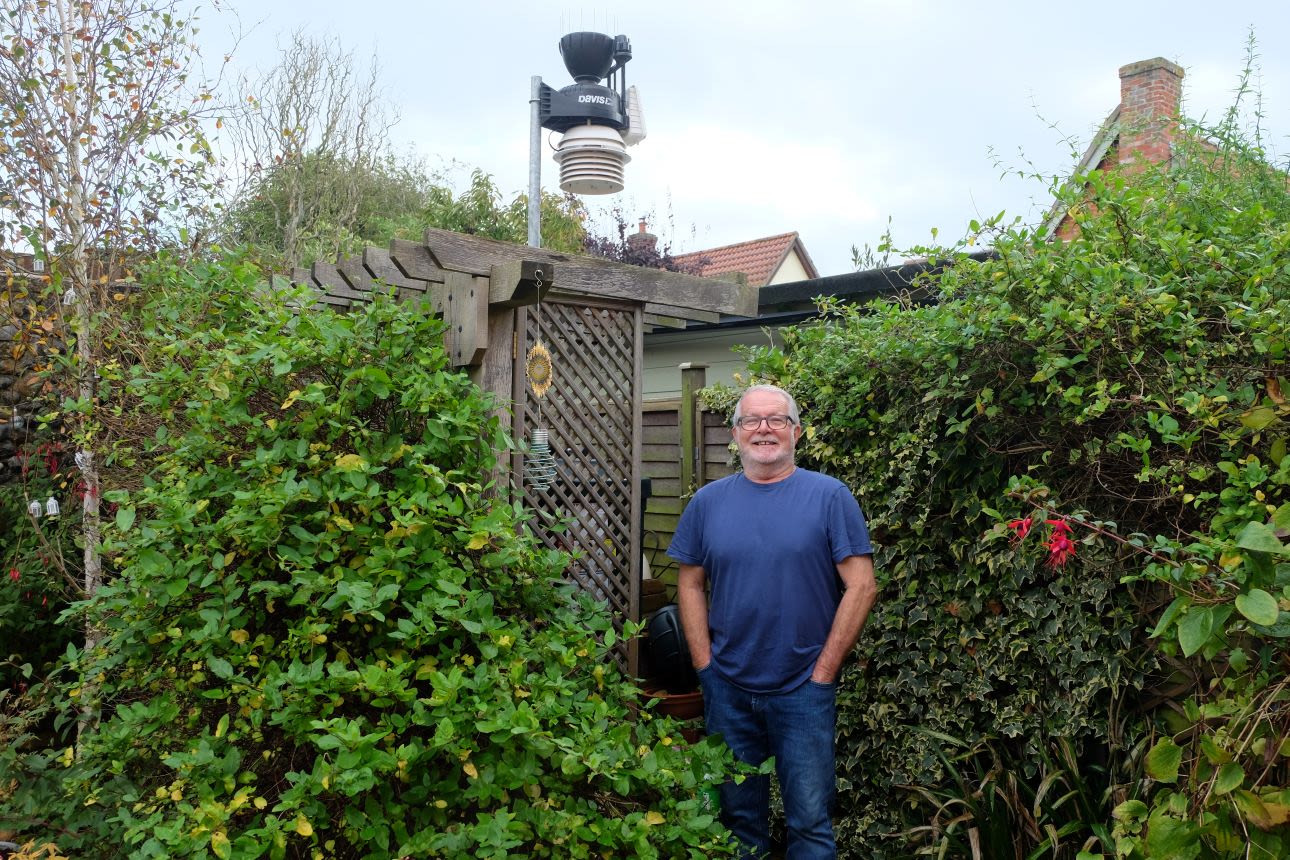 Richard standing in his garden by his weather station, which measures temperature, humidity, rainfall, and sunshine amounts.