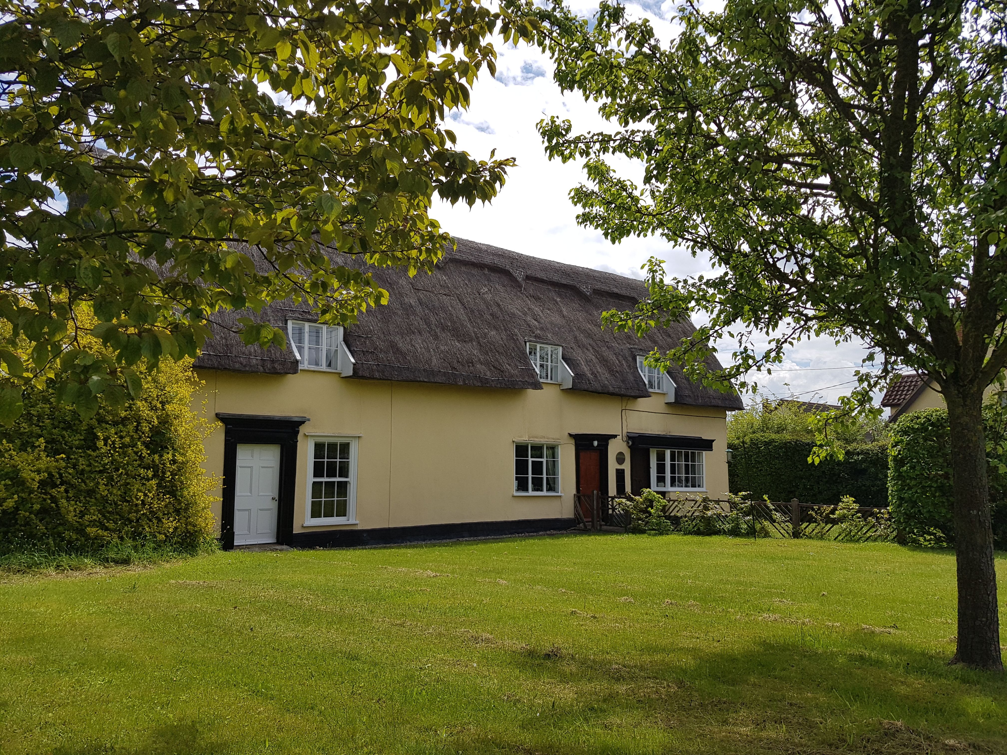 A modern photograph of a thatched cottage and garden, once called “Minerva Cottage”
