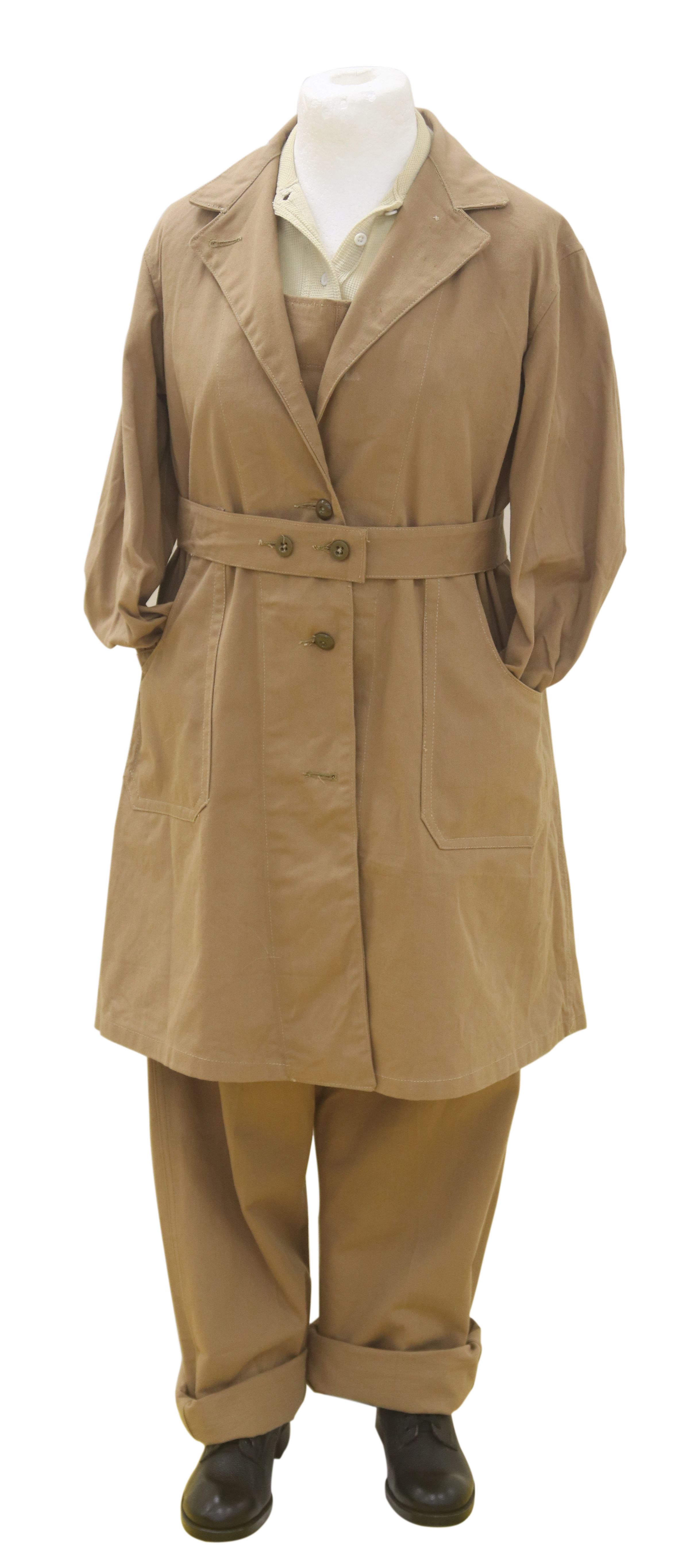 Colour photograph of a mannequin wearing a knee-length light brown cotton overcoat with a belt at the waist, over the light brown cotton dungarees and black gumboots.