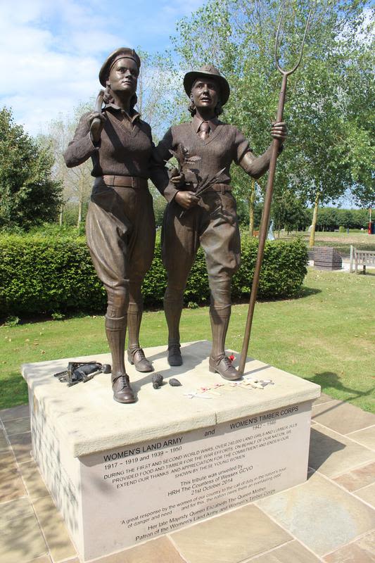 Colour photograph of a memorial composed of a light coloured stone plinth, topped by two life-size bronze figures of a Land Girl and a Lumber Jill