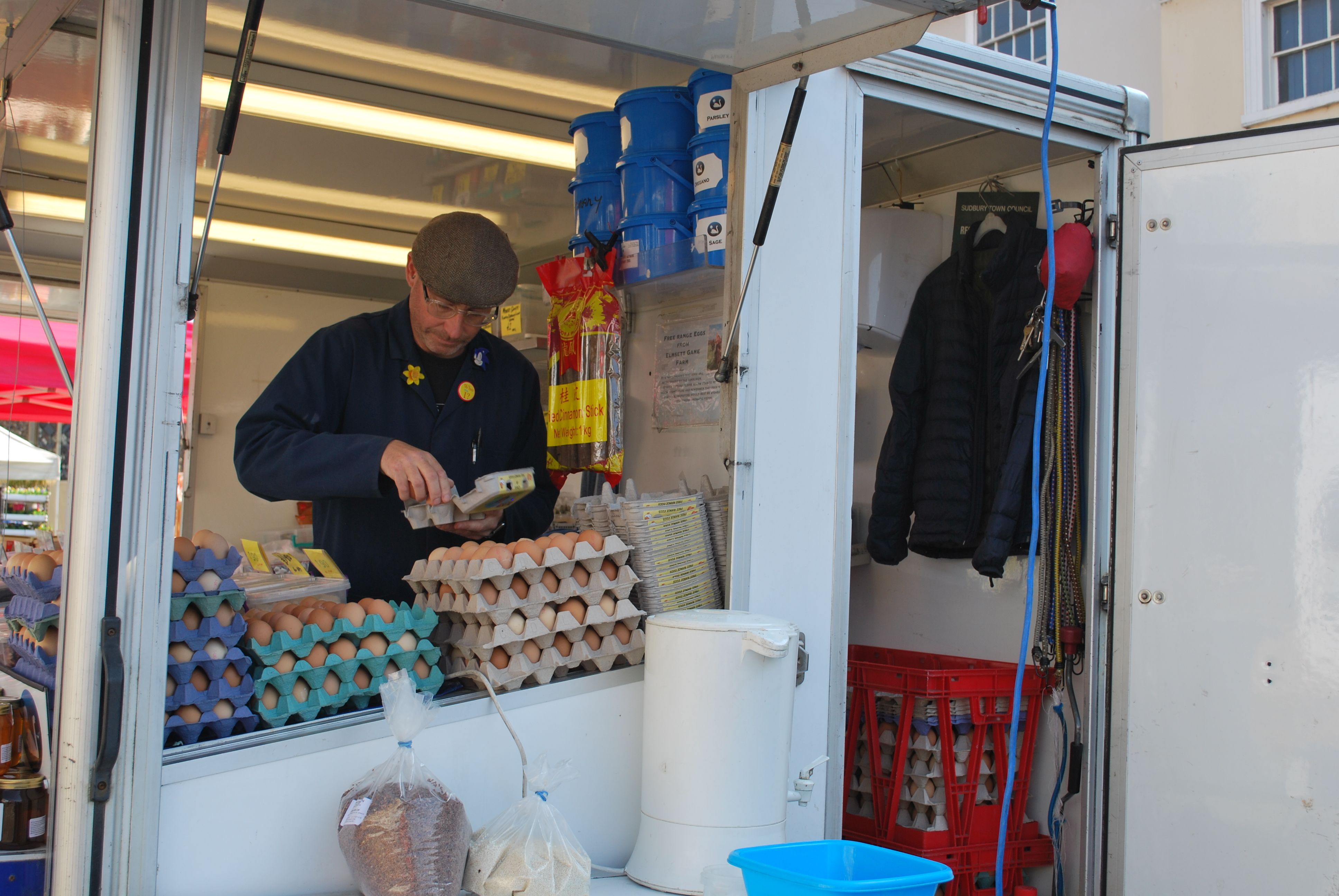 Photo of a man in blue overalls and a flat cap taking eggs from large trays and putting them into a half-dozen egg box