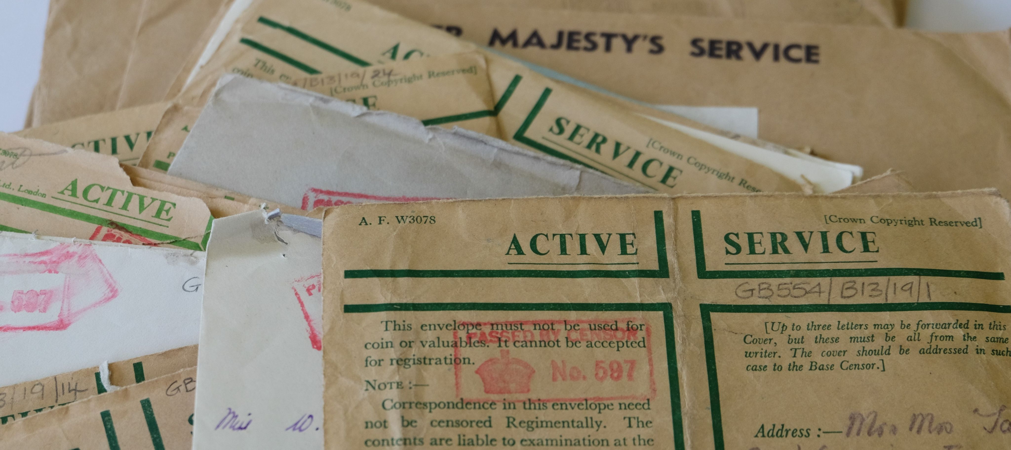 A pile of worn envelopes scattered on a table. They are cream and buff in colour, and a green heading saying Active Service, and a read stamp to indicate they have passed an army censor