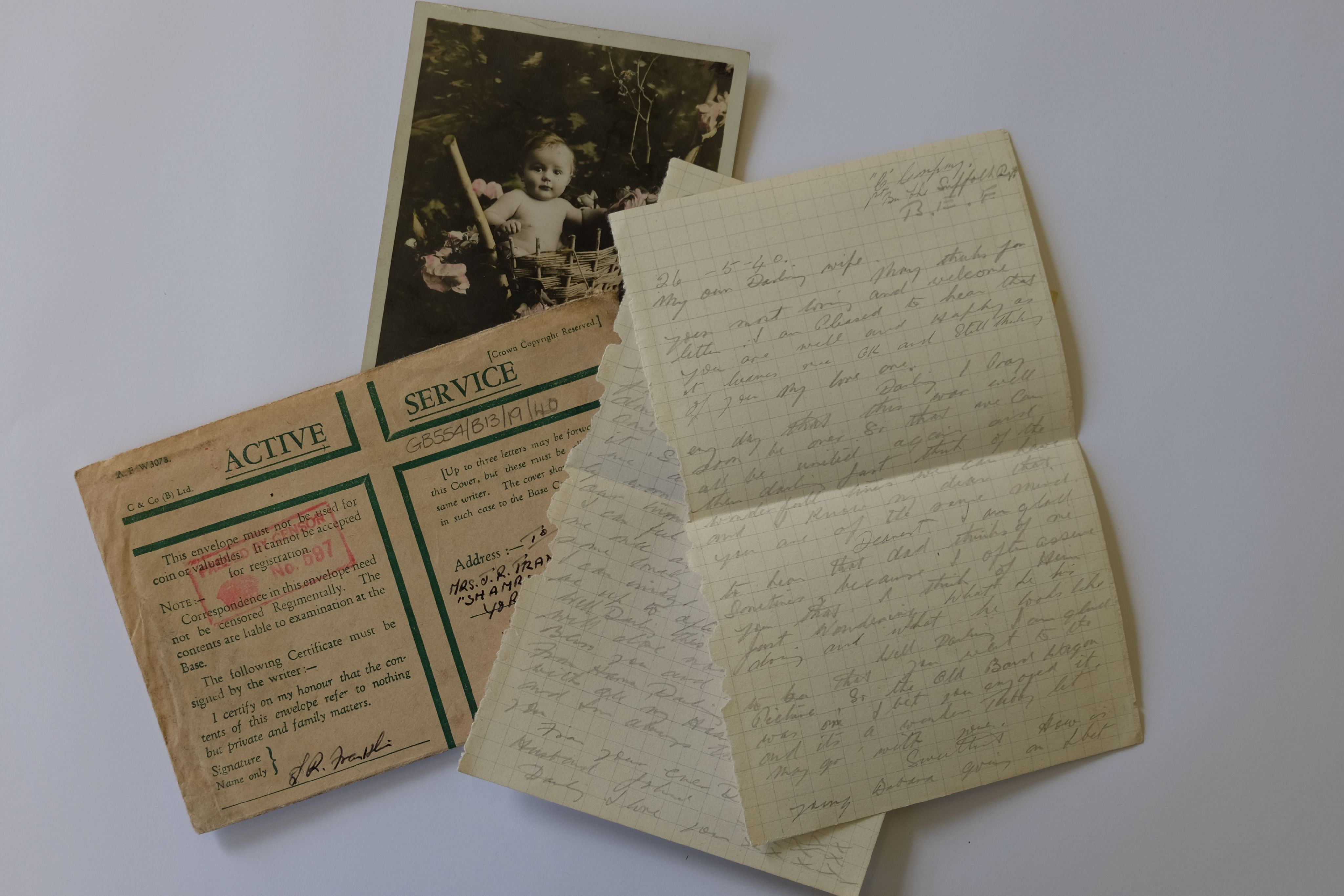 Photograph showing a wartime letter, written on grid paper in pencil. There is also a buff envelope headed Active Service in green ink, and a photograph of a baby in a pram.